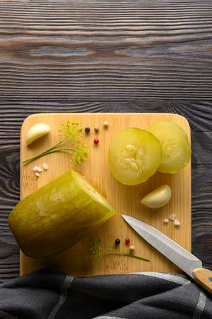 Healthy fermented vegan food. Sliced fermented pickled cucumber and spices on a cutting board. Rustic wooden background. Top view, copy space, vertical orientation.の写真素材