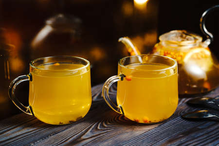 Hot warming healthy drink with sea buckthorn berries. Two glass cups with berry tea on the windowsill. Rainy autumn evening.の写真素材