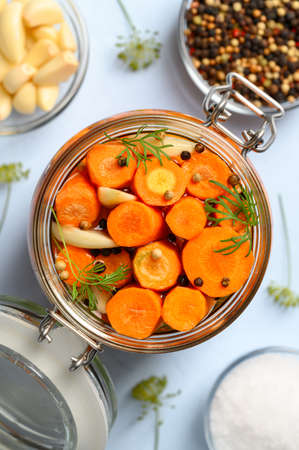 Healthy vegan food. Homemade fermented carrots with garlic, dill and pepper in a glass jar. Light blue background. Top view, close-up, vertical orientation.の写真素材