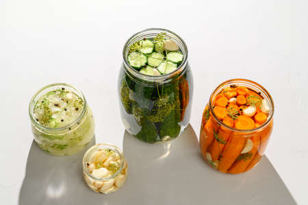 Healthy vegan food. Homemade fermented vegetables cucumbers, carrots, cabbage and garlic in glass jars. Light gray background. Top view, hard light.の写真素材