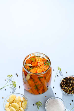 Healthy vegan food. Homemade fermented carrots with garlic, dill and pepper in a glass jar. Light blue background. Top view, vertical orientation, hard light.の写真素材