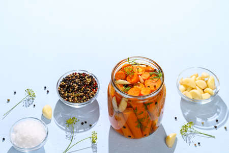 Healthy vegan food. Homemade fermented carrots with garlic, dill and pepper in a glass jar. Light blue concrete background. Top view, space for text, hard light.の写真素材