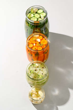 Healthy vegan food. Homemade fermented vegetables cucumbers, carrots, cabbage and garlic in glass jars. Light background. Top view, vertical orientation, hard light.の写真素材