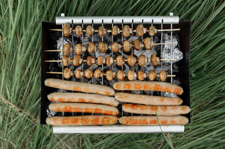 Top view of sausages and mushrooms on the grill grate. Charcoal cooking during a picnic.の写真素材