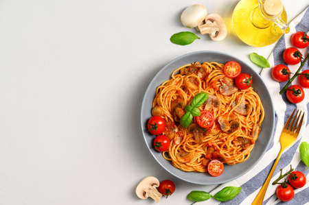 Traditional Italian cuisine. Plate with spaghetti, tomato sauce, cherry tomatoes, mushrooms and basil on a light gray background. Copy space, top view.の写真素材