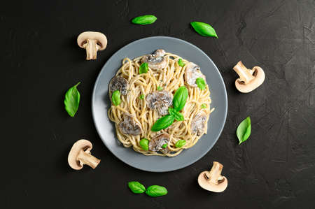 Spaghetti with creamy sauce, mushrooms and basil leaves on a dark background. Homemade Italian pasta with mushrooms in a gray plate. View from above.の写真素材