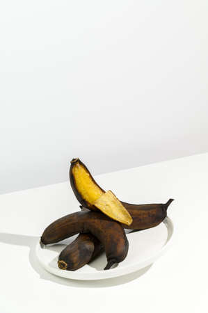 Waste food concept. Stale ugly bananas in a plate white background. Creative isometric style, copy space. Flying objects.の写真素材