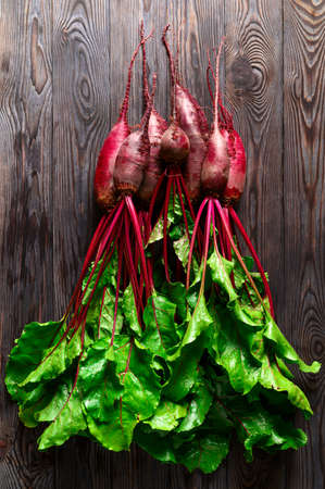 Raw beets with green tops on a dark wooden background. Eco food, rustic style. Top view, vertical...
