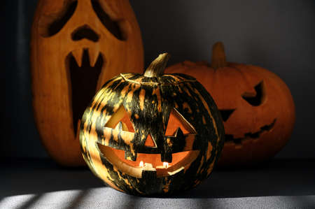 Halloween holiday background. Three Spooky Halloween pumpkins on the table, illuminated by sunlight through the jalousie. Shadows.の写真素材