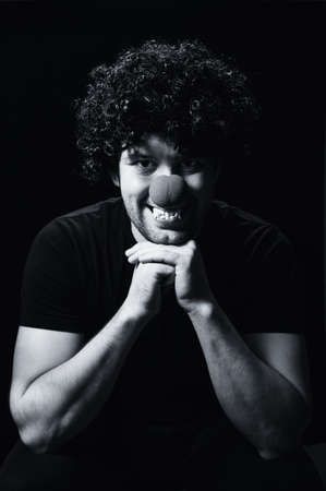 An angry male vampire in black clothes and a wig, bared his teeth, looks at the camera on a black background. Black and white photography. Vertical orientationの写真素材