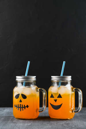 Iced pumpkin cocktails in glass jars decorated with scary faces on the chalkboard, black background. Halloween Party mocktails. Vertical orientation, copy spaceの写真素材