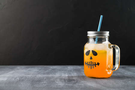 Iced pumpkin cocktail in glass jar decorated with scary face on the chalkboard, black background. Halloween Party mocktail. Copy spaceの写真素材