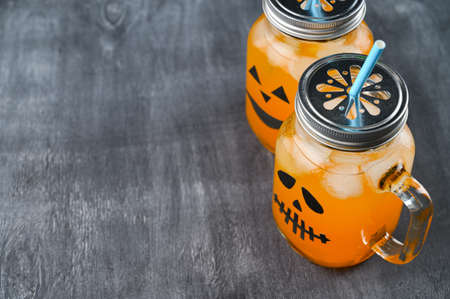 Iced pumpkin cocktails in glass jars decorated with scary faces on the chalkboard. Halloween Party mocktails. Copy spaceの写真素材