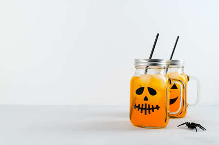 Iced pumpkin cocktails in glass jars decorated with scary faces on the gray table, white background. Halloween Party mocktails. Copy spaceの写真素材