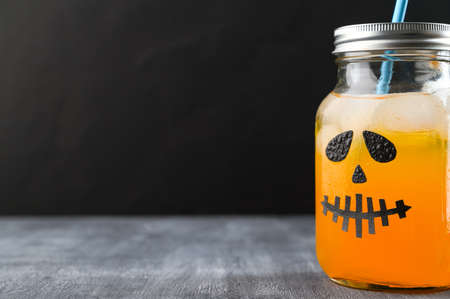 Iced pumpkin cocktail in glass jar decorated with scary face on the chalkboard, black background. Halloween Party mocktail. Copy spaceの写真素材