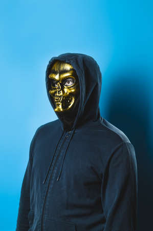 Portrait of a man in a skull mask with a hood on a blue background. Halloween party costume. Vertical orientationの写真素材