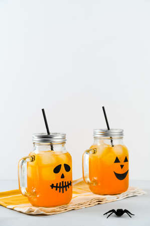 Iced pumpkin cocktails in glass jars decorated with scary faces on the gray table, white background. Halloween Party mocktails. Vertical orientation, copy spaceの写真素材
