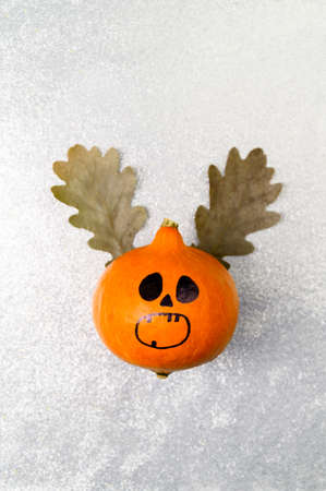 Top view Halloween pumpkin with painted face and horns made from autumn leaves on a shiny silver background. Portrait Orientation, Copy Space, Flat Lay.の写真素材