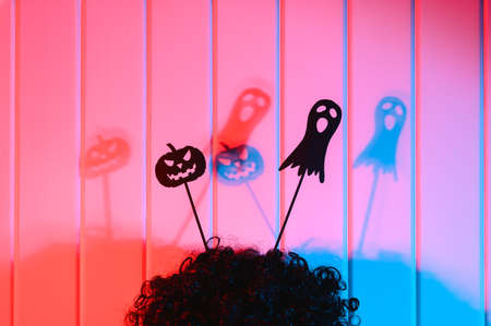 Halloween decorations. Scary black paper dolls of pumpkin and ghost on a wig in the form of horns on the background of a wooden wall. Neon lighting. Close-up.の写真素材