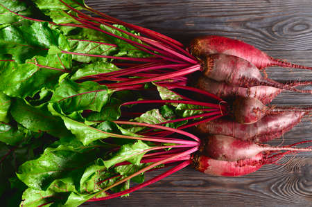 Raw beets with green tops on a dark wooden background. Eco food, rustic style. Top view