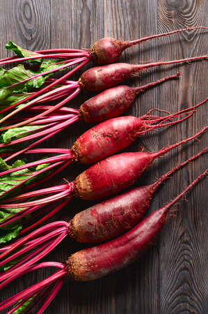 Raw beets with green tops on a dark wooden background. Eco food, rustic style. Top view, vertical orientation.の写真素材