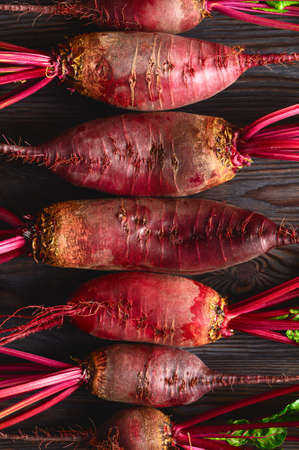 Raw beets with green tops on a dark wooden background. Eco food, rustic style. Top view, vertical orientation.の写真素材