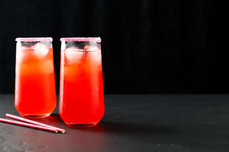 Refreshing summer mocktails with ice cubes. Two tall glasses of iced red juice with straws on dark background. Copy spaceの写真素材