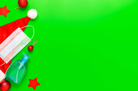 New normal christmas concept. Top view of medical mask, sanitizer bottle, Santa hat and Christmas decorations on green background. Minimal composition. Copy space, flat layの写真素材