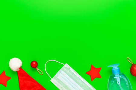 New normal christmas concept. Top view of medical mask, sanitizer bottle, Santa hat and Christmas decorations on green background. Minimal composition. Copy space, flat layの写真素材