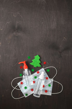 Christmas era covid concept. Medical protective masks, sanitizer bottles and Christmas decorations on a dark brown background. Flat Lay, copy space, minimalism. Vertical orientationの写真素材