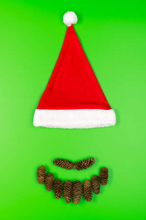 Santa Claus face made of fir cones and a traditional red hat on a green background. Minimal Christmas concept. Flat lay, vertical orientation.の写真素材