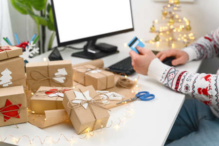 Christmas shopping online. Unrecognizable Man Hands holding Credit Card buying presents by using a computer. The man wearing a sweater shopping online at the home office. Long-distance gifting.の写真素材
