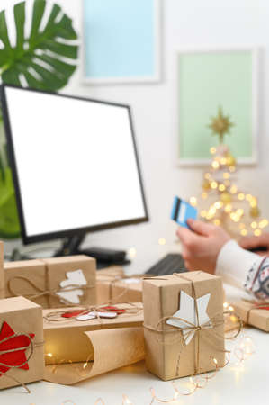 Christmas shopping online. Unrecognizable Man Hands holding Credit Card buying presents by using a computer. The man wearing a sweater shopping online at the home office. Long-distance gifting.の写真素材