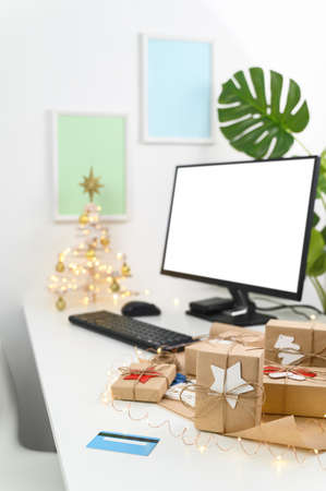 Christmas Shopping online with a credit card. Christmas gifts and a computer monitor on a table in a home office. Winter holidays sales. Long-distance gifting.の写真素材