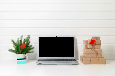 Christmas online shopping concept. Laptop, gifts, credit card and spruce branches on the background of a white wooden wall. Copy space, minimal style. Winter holidays sales.の写真素材