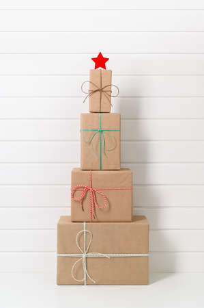 Alternative Christmas tree made from gift boxes with a white star on the background of a white wooden wall. Vertical orientation. Simple, minimal styleの写真素材