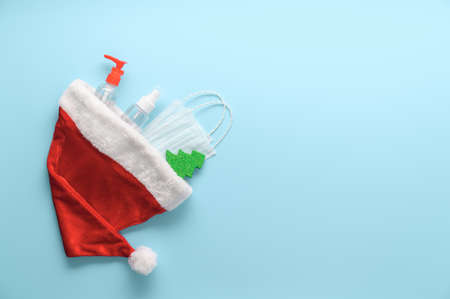 New normal christmas concept. Top view of medical masks, sanitizer bottles, Santa hat and Christmas decorations on pastel blue background. Minimal composition. Copy space, flat layの写真素材