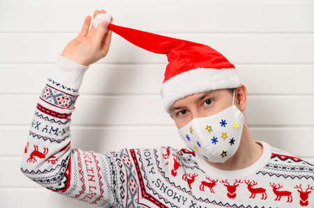 Close up portrait of adult person wearing white medical fabric mask, Santa hat and sweater, isolated over white background. Stay home. Christmas coronavirus conceptの写真素材