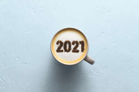 New year background. Number 2021 on frothy surface of cappuccino in coffee cup on pastel blue...