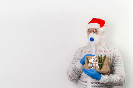 Delivery man holding gift box in eco-friendly reusable packaging on white background. He wearing protection costume, face mask, glasses and medical rubber gloves safety form coronavirus. Safe deliveryの写真素材