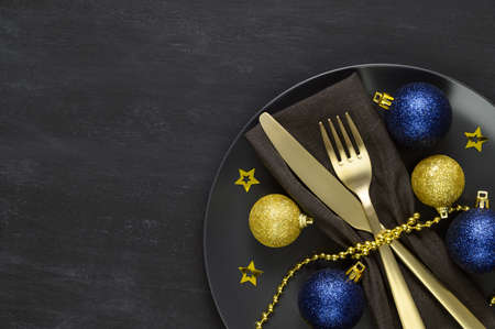 Festive table setting with black plate, golden cutlery and xmas decorations on dark chalkboard. Christmas table setting. Flat lay, top view. Minimal style, copy spaceの写真素材
