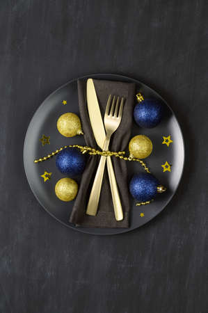 Festive table setting with black plate, golden cutlery and xmas decorations on dark chalkboard. Christmas table setting. Flat lay, top view. Minimal style, copy spaceの写真素材