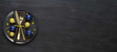 Festive table setting with black plate, golden cutlery and xmas decorations on dark chalkboard. Christmas table setting. Flat lay, top view. Minimal style, copy space, bannerの写真素材