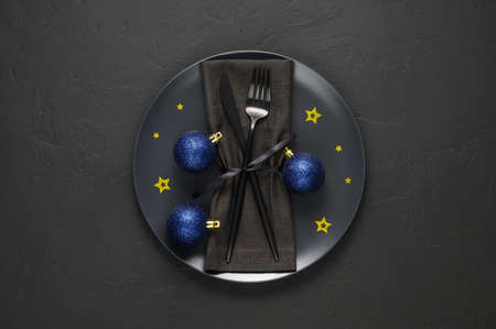 Festive table setting with black plate, cutlery and blue xmas balls on dark tabletop. Christmas table setting. Flat lay, top view. Minimal style, copy spaceの写真素材