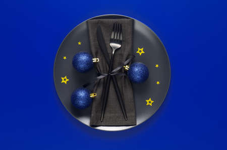 Festive table setting with black plate, cutlery and xmas balls on blue background. Christmas table setting. Flat lay, top view. Minimal styleの写真素材