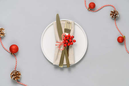 Festive table setting with white plate, golden cutlery and xmas decorations on light gray tabletop. Christmas table setting. Flat lay, top view. Minimal styleの写真素材