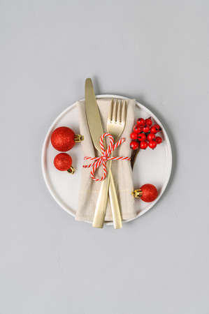 Festive table setting with white plate, golden cutlery and xmas decorations on light gray tabletop. Christmas table setting. Flat lay, top view. Minimal style, copy spaceの写真素材