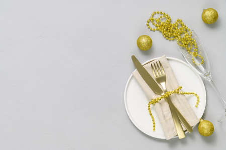 Festive table setting with white plate, golden cutlery, wine glass and gold xmas decorations on light gray tabletop. Christmas table setting. Flat lay, top view. Minimal style, copy spaceの写真素材