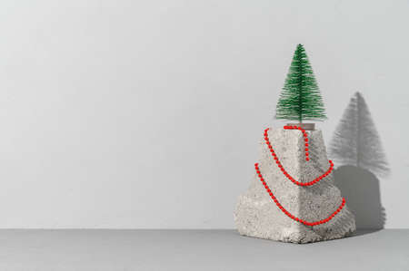 Conceptual festive card with trendy stone podium, miniature Christmas tree and red beads on gray background. Copy space, place for text. Minimalist styleの写真素材