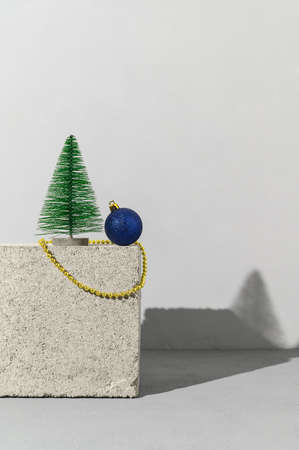 Conceptual festive composition with trendy stone podium, miniature Christmas tree, gold beads and blue ball on gray background. Copy space, place for text, vertical orientation. Minimalist styleの写真素材